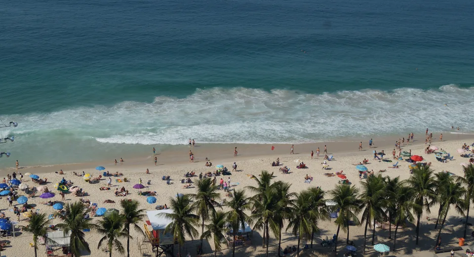 Vista elevada de una playa de Río de Janeiro con olas, bañistas, sombrillas y palmeras