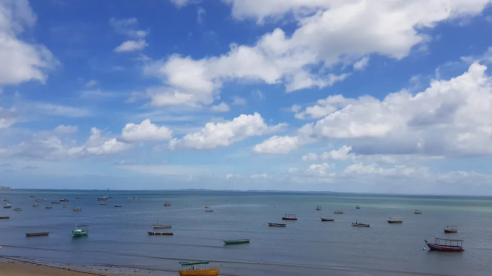 Pequeñas barcas sobre aguas costeras tranquilas bajo un cielo azul con nubes en Brasil