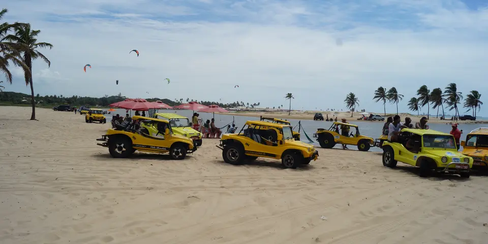 Gelbe Strandbuggys am Wasser und Kites am Himmel in Cumbuco bei Fortaleza