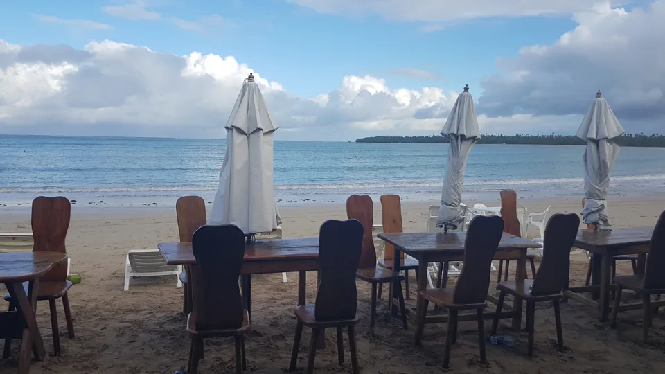 Restaurant tables and closed parasols on the sand facing the sea at Morro de São Paulo